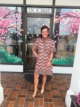 Load image into Gallery viewer, A woman stands in front of a storefront doorway wearing a short-sleeve patterned dress with a brown and pink abstract design, paired with metallic gold platform sandals. The storefront has pink cherry blossom tree decals on the windows and a brick floor.