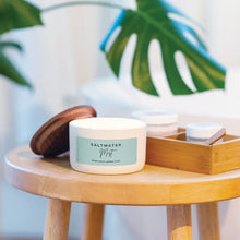 Load image into Gallery viewer, Candle labeled 'Saltwater Mist' on a wooden table with a blurred plant in the background